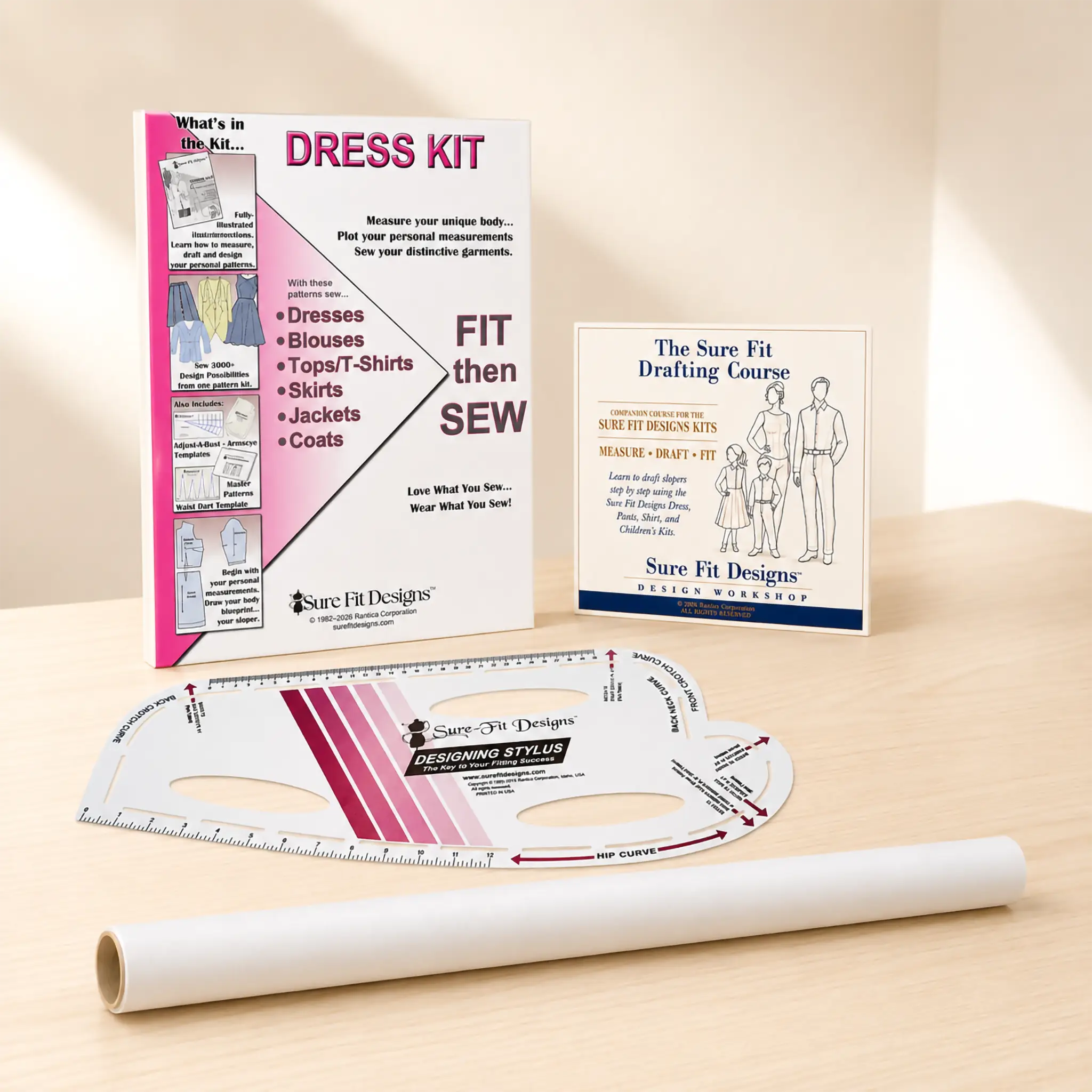 A sewing dress kit set displayed on a light wood surface, including a printed instruction booklet, a drafting course card, a curved measuring ruler, and a roll of white fabric.