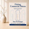 A Fitting Commercial Patterns course displayed vertically on a light maple table with a small flower arrangement on the left