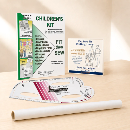 A sewing pattern drafting and fitting kit for children's clothing displayed on a light wood surface, including a printed 'Children's Kit' booklet, a drafting course booklet, a curved ruler, and a roll of tracing paper or vellum.