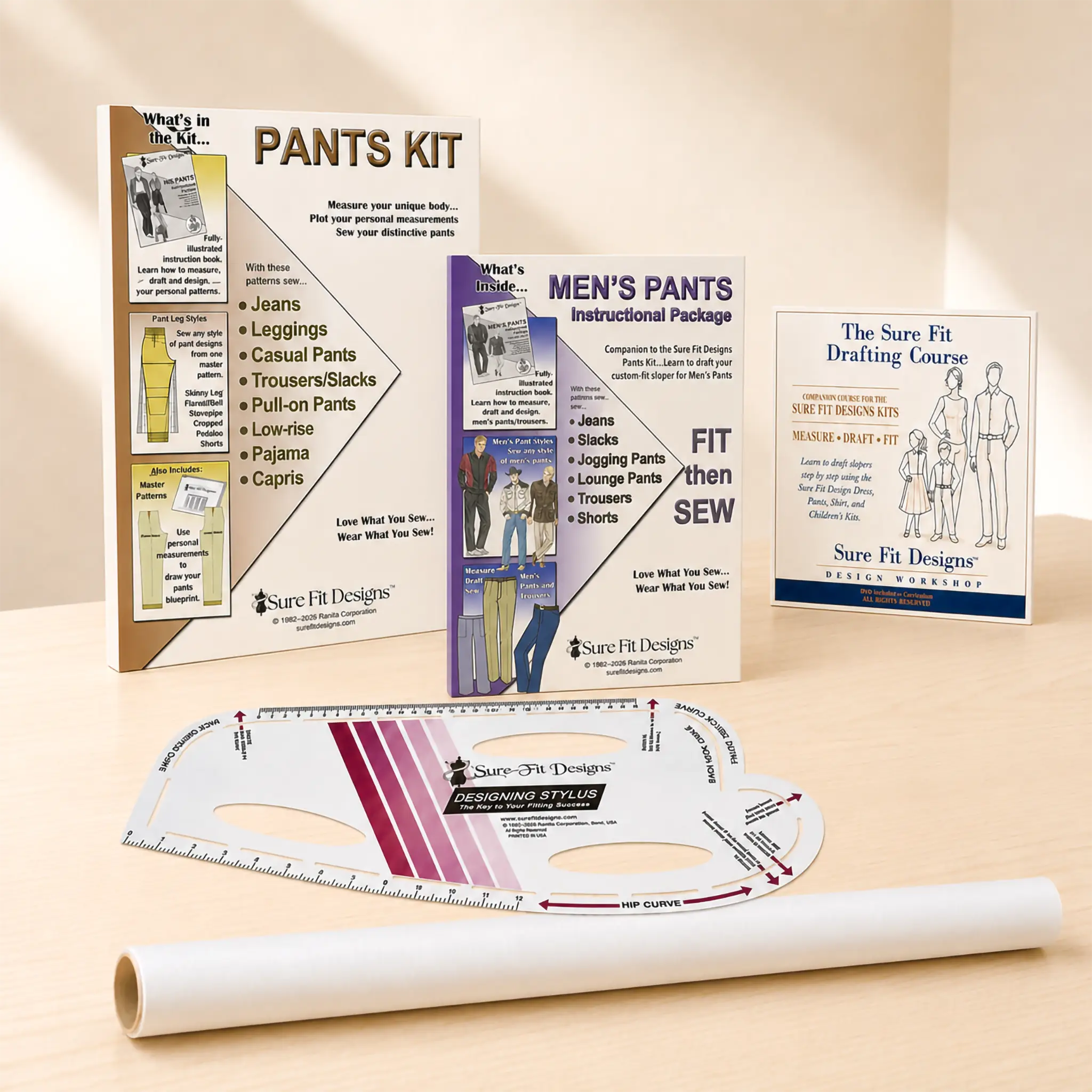 Sure Fit Designs Pants Kit. Sewing pattern drafting and fitting kit displayed on a light wood surface with a beige background. Includes the pants, men's pants and drafting instruction booklets, a curved ruler, and a roll of tracing paper / vellum.
