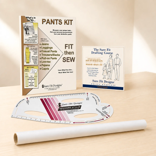 A pants pattern drafting and fitting kit set on a light wood surface with a warm beige background. Includes a roll of tracing paper or vellum, a curved ruler, and two printed booklets: one for 'Pants Kit' and the other 'The Sure Fit Drafting Course'.
