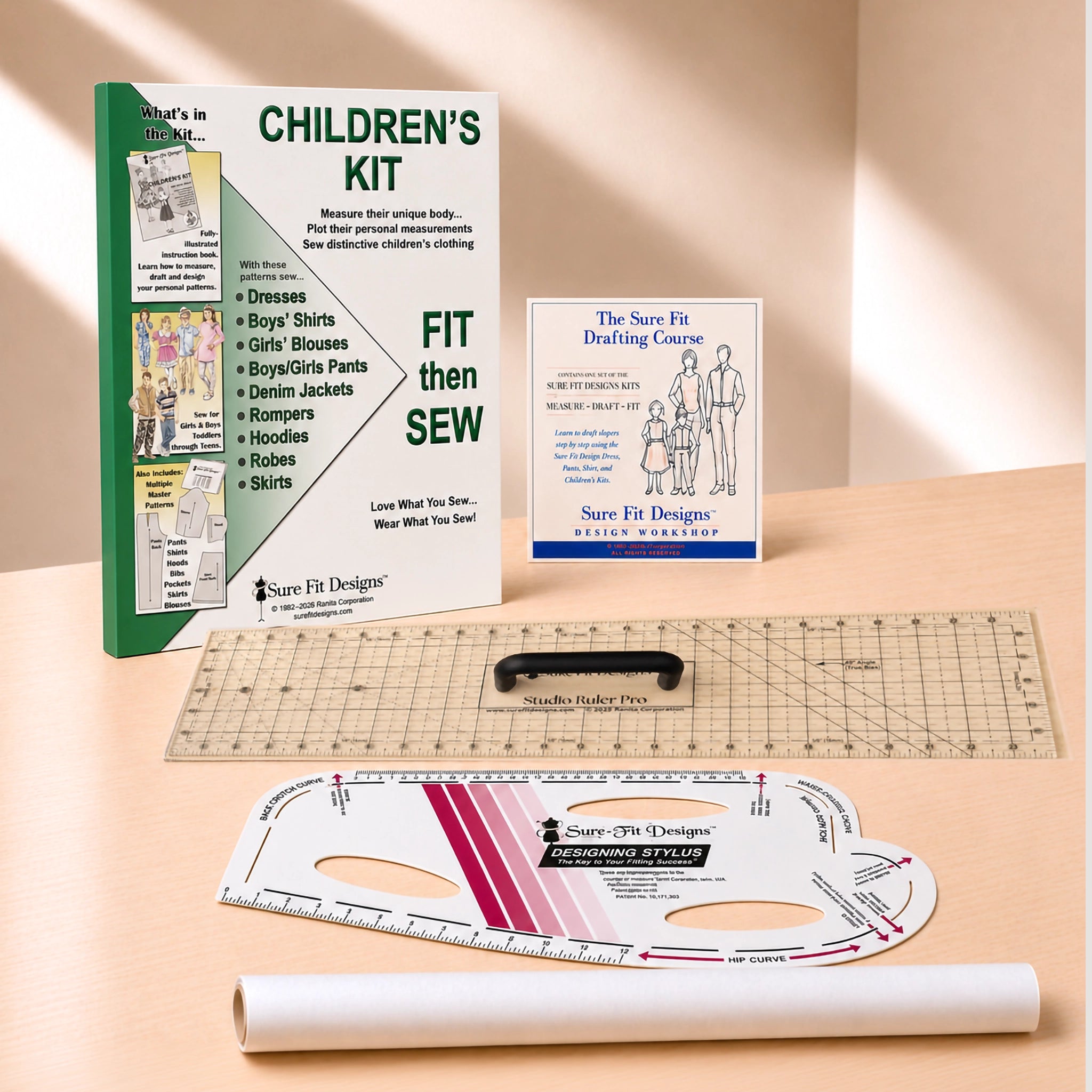 A children's sewing kit laid out on a light wood surface, including a green and white instruction booklet, a small blue-and-white guide card, a clear gridded quilting ruler, a white curved measuring template, and a rolled white paper sheet. Visible branding includes Sure Fit Designs and The Save Fit Designs.