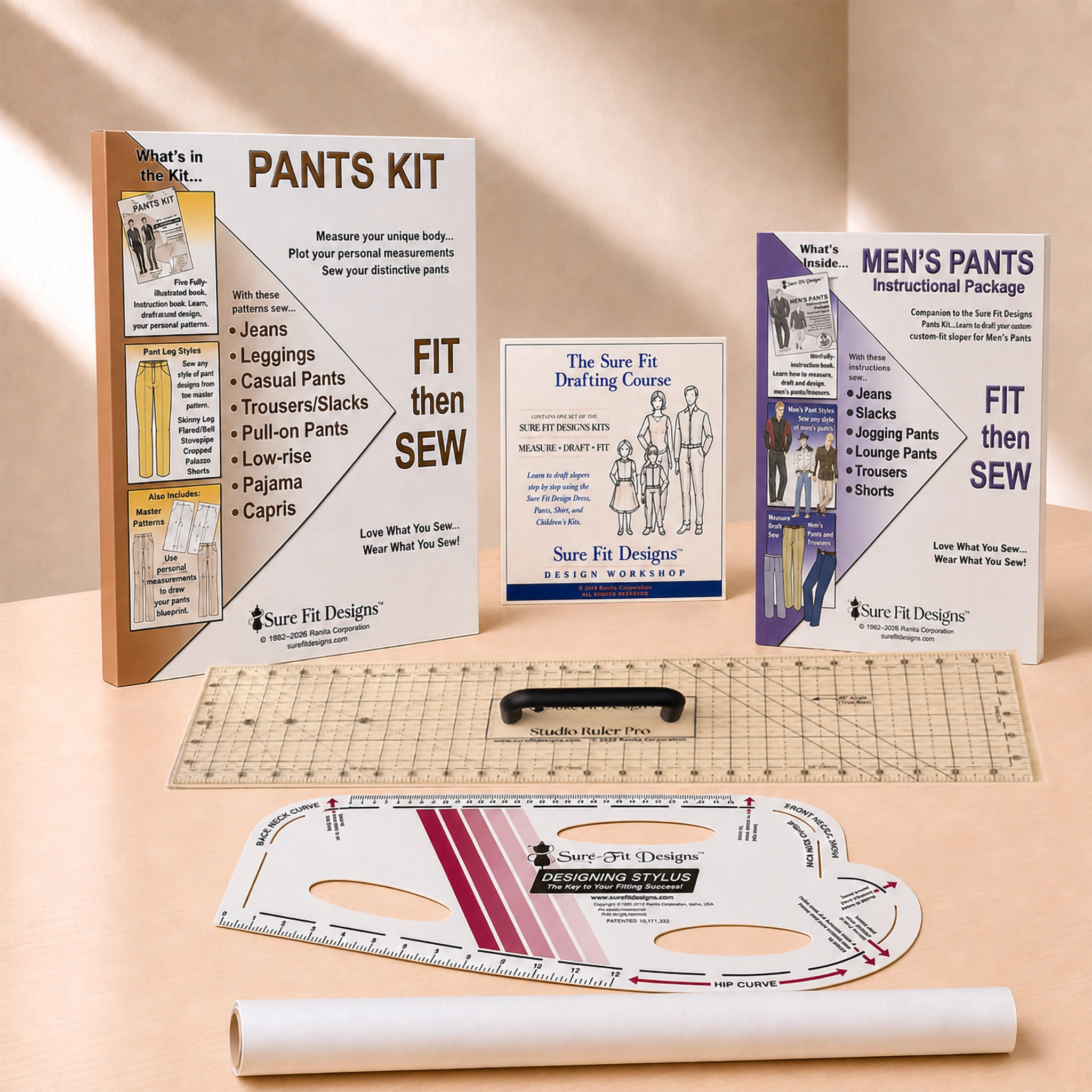 A sewing and measurement kit set displayed on a beige surface, including a 'PANTS KIT' manual, 'MEN'S PANTS INSTRUCTIONAL PACKAGE', a clear marked square grid, a black rotary cutter, a white and pink curved measuring template, and a white roll of paper. The brand 'Sure Fit Designs' is clearly visible on the manuals and tools.