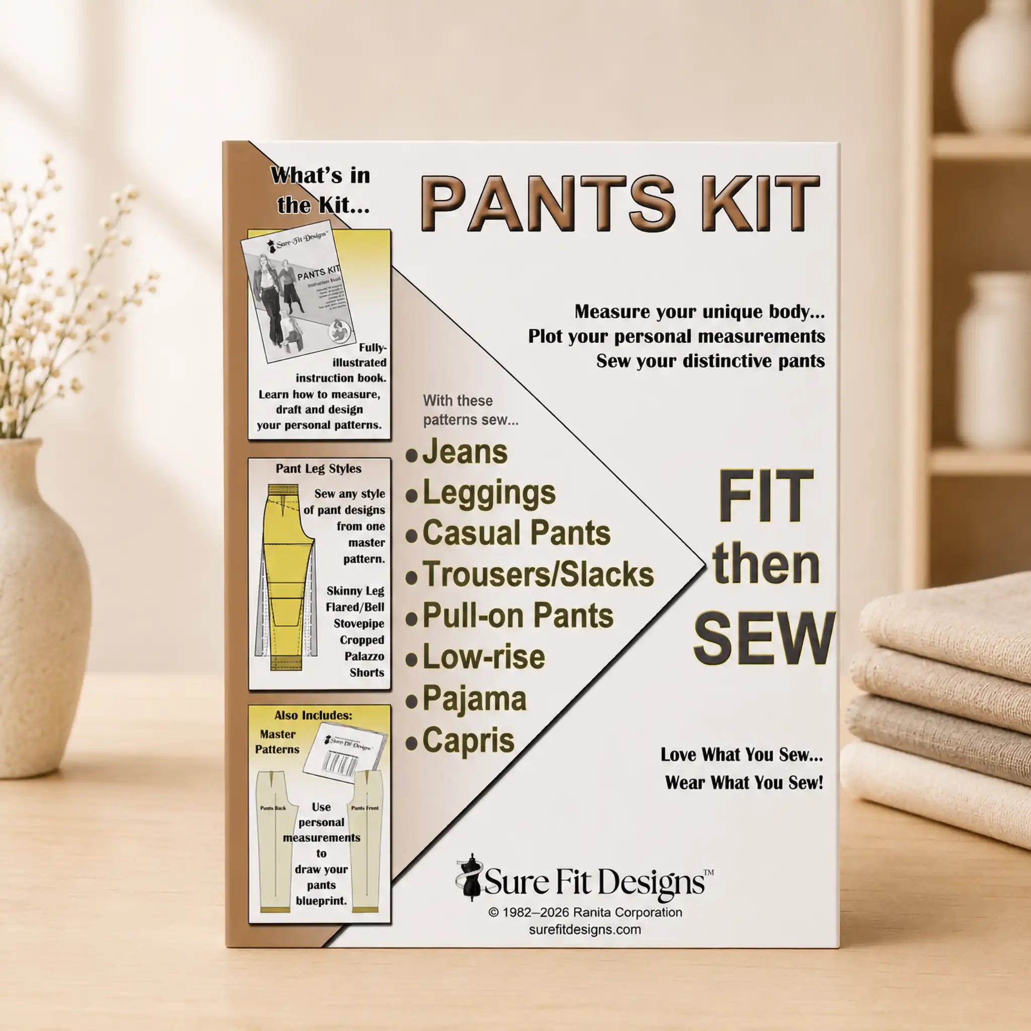 A 'Pants Kit' instruction booklet by Sure Fit Designs stands upright on a wooden surface. The booklet features a white and beige cover with black and brown text, detailing how to measure and sew distinctive pants.