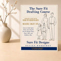 The Sure Fit Drafting Course displayed vertically on a light maple table with a small flower arrangement on the left
