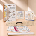 A sewing pattern kit and fitting tools arranged on a warm beige studio surface. Visible items include a 'PANTS KIT' instruction booklet, two Sure Fit Designs course cards, a clear acrylic ruler, a curved measuring template, and a white fabric roll.